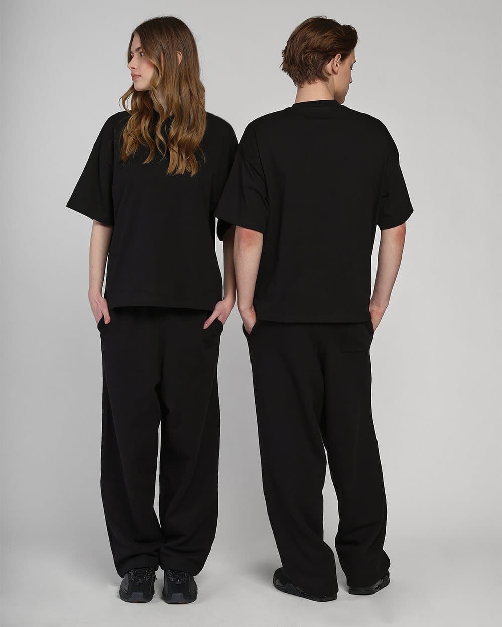Two models in black tops and trousers, one seen from behind, one from the front