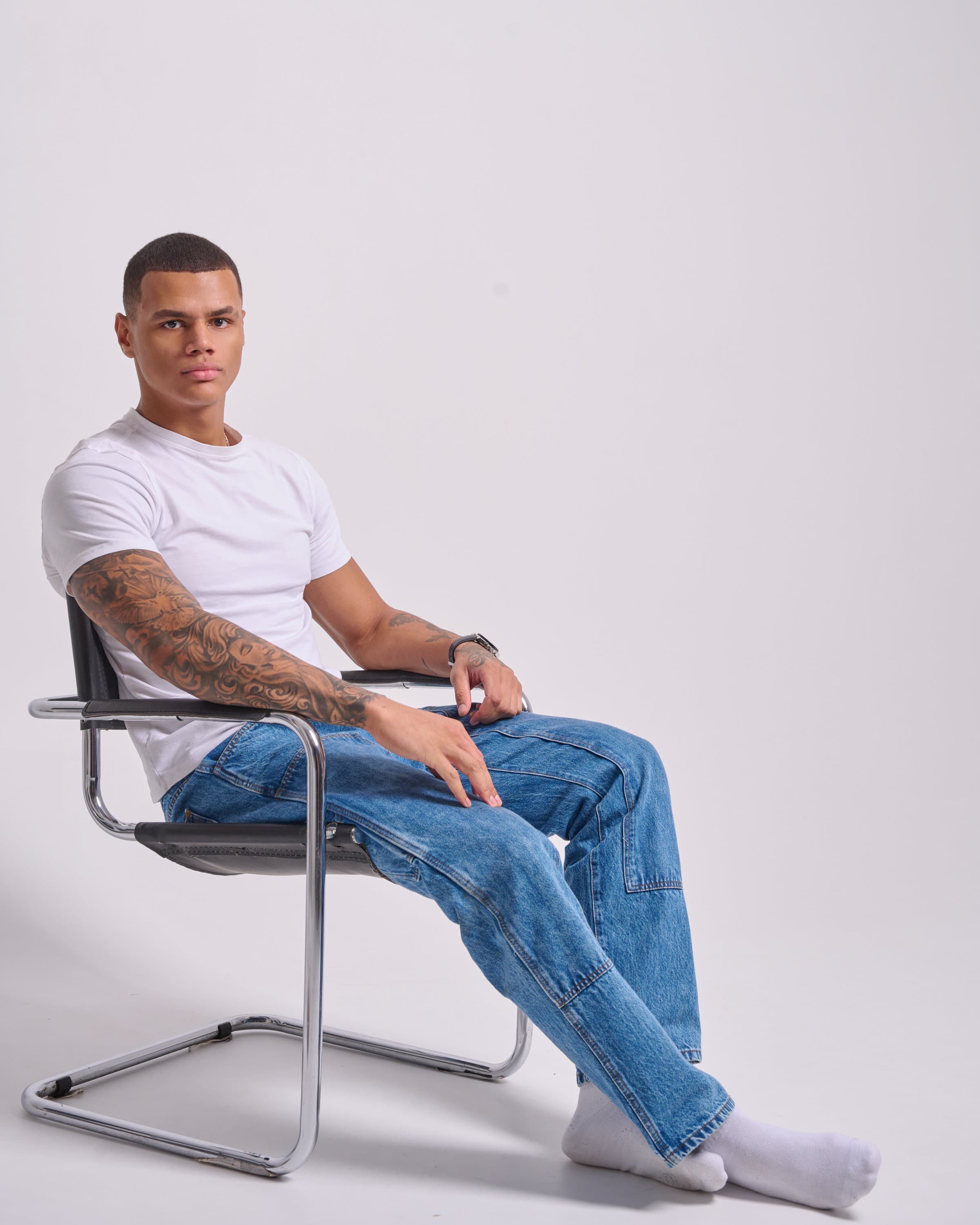 Model in a white T-shirt and blue jeans sitting on a chrome chair in the studio