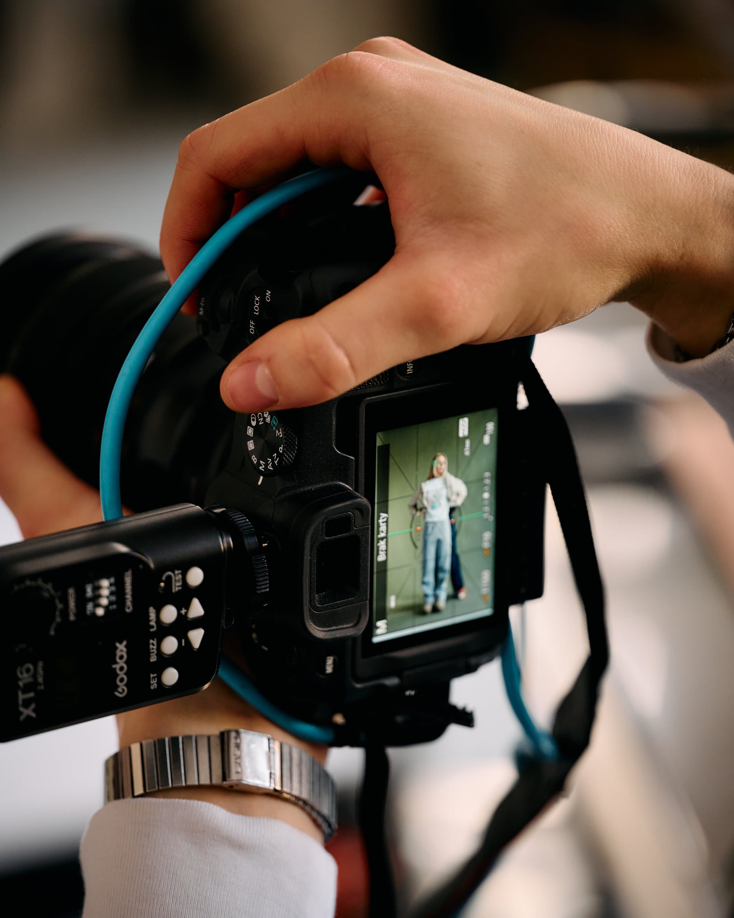 Close-up of hands holding a camera, its screen showing a model on set