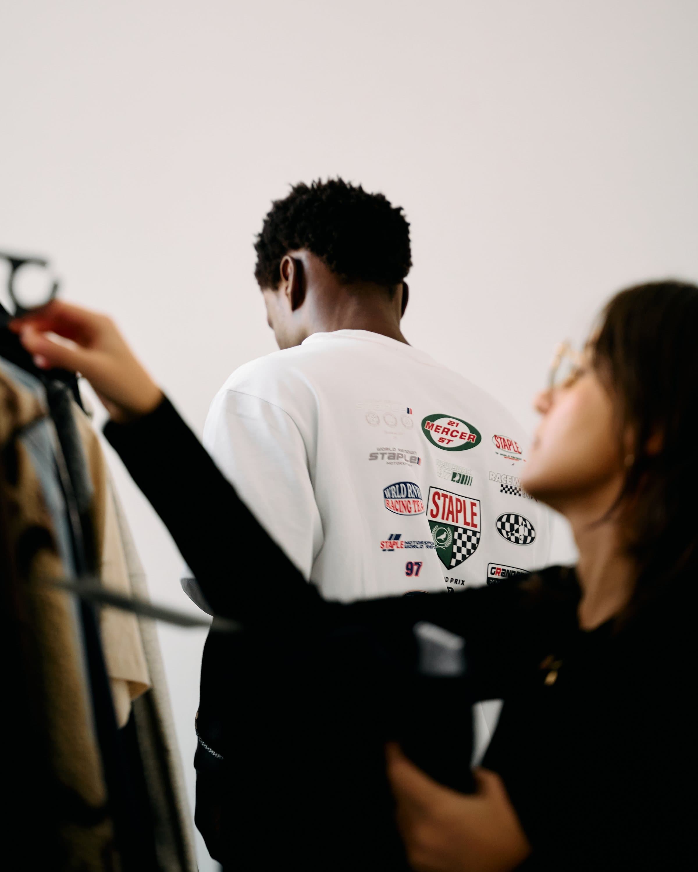 Stylist adjusting a model's jacket on set beside a clothing rail