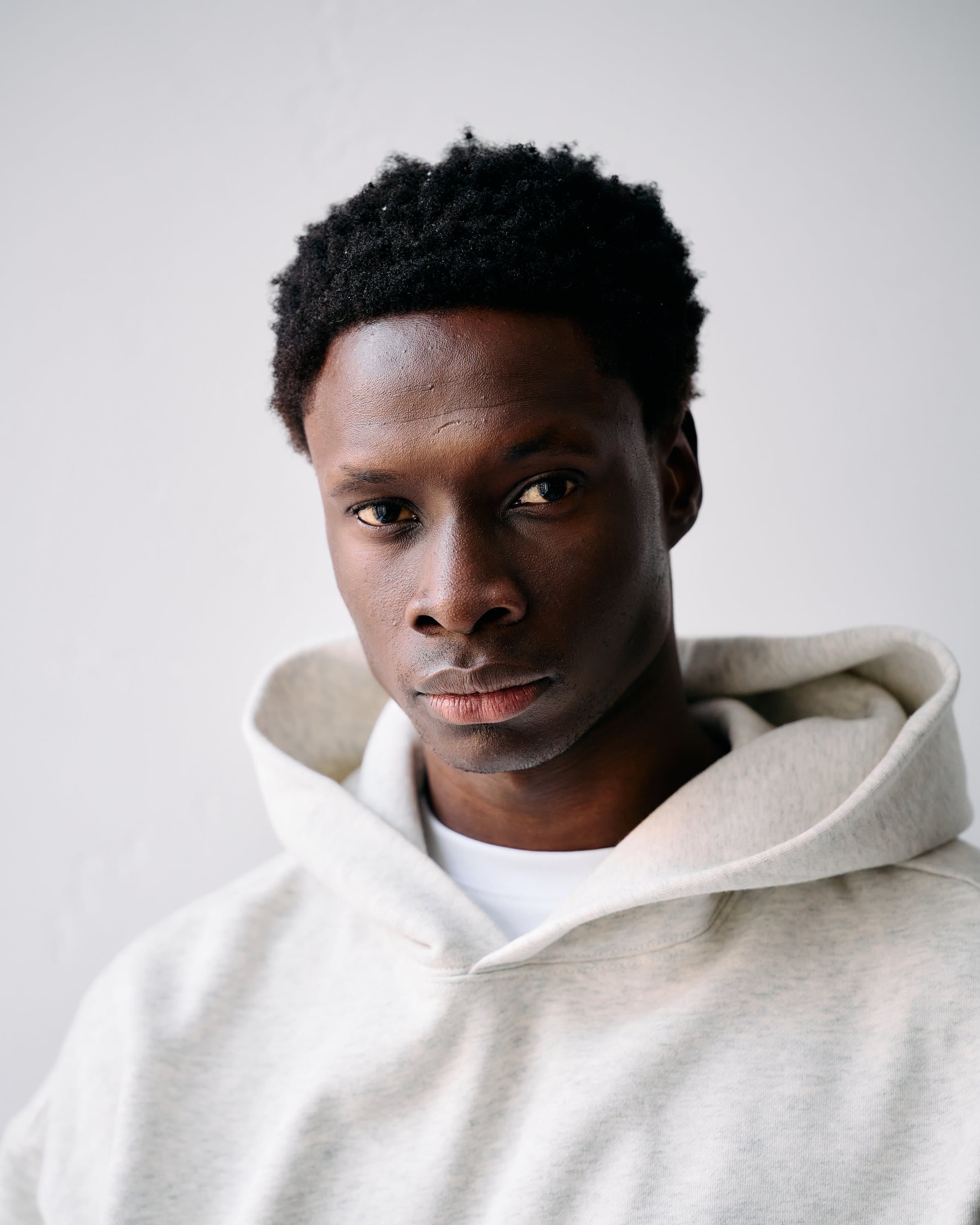 Studio portrait of a young man in an oatmeal hoodie against a white wall