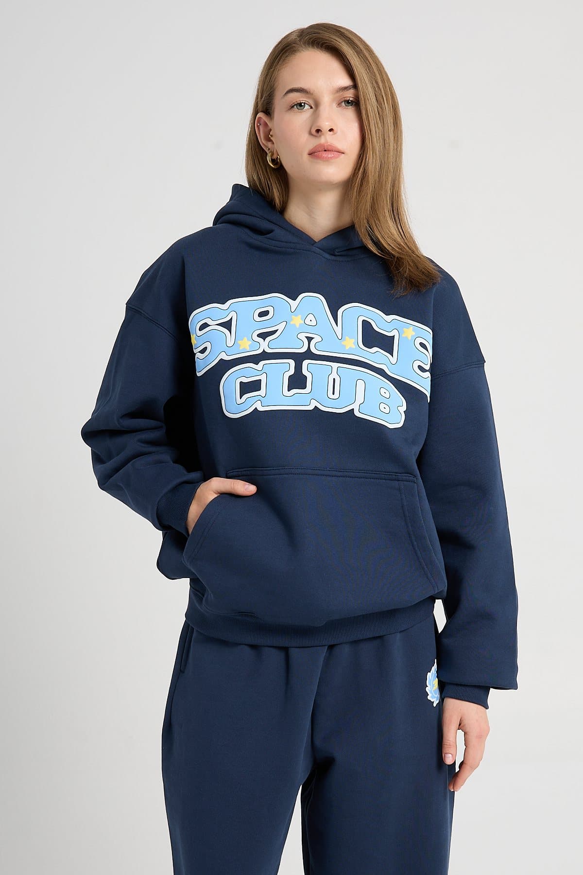 Model in a navy hoodie and joggers with a light blue print on a light studio backdrop